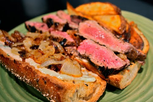 Skirt steak sandwich caramelized withn onions served in the plate.