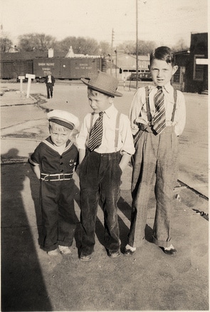 Vintage three young boys dressed up and standing in the ground.