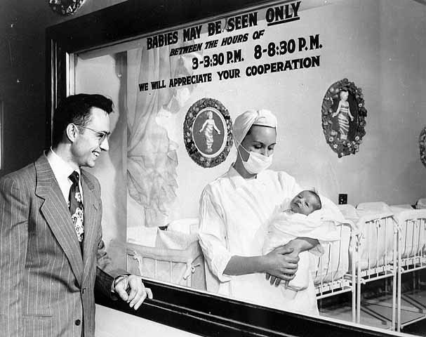 Vintage man looking at newborn baby in infant ward of hospital.