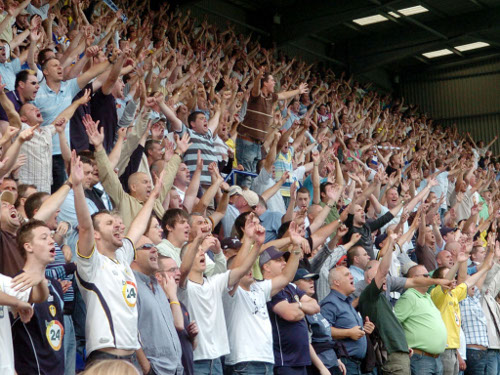 Fans in the stadium standing, yelling and cheering.