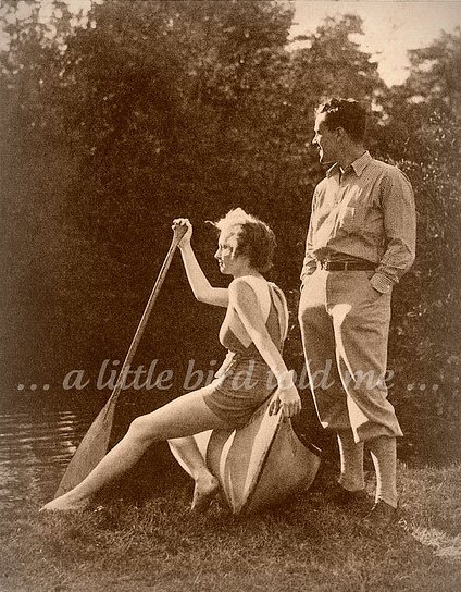 Vintage couple at river bank while woman sitting on canoe holding paddle and man standing.