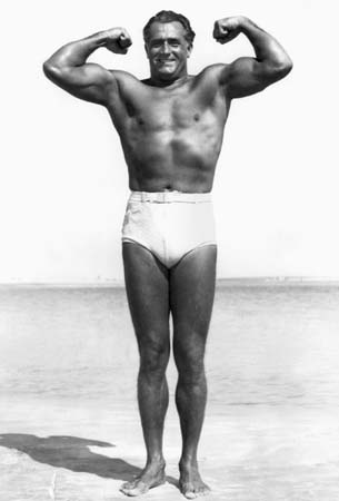 Vintage Charles Atlas giving muscle pose on beach. 