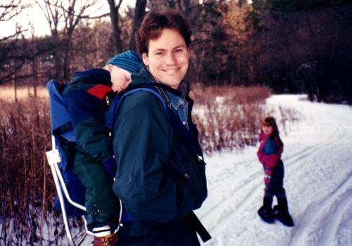 A man with kid on his back with a girl on a snowy track.