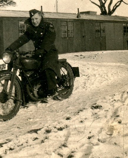 Vintage man wearing overcoat on motorcycle in snow.