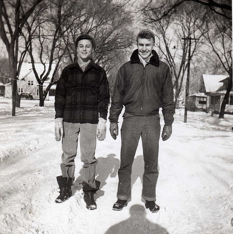 Vintage boys standing in a snowy road wearing coats, hats and gloves.