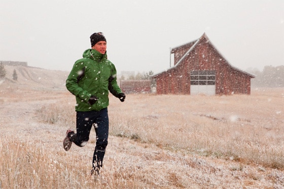 Man in layers running through field while snowing.