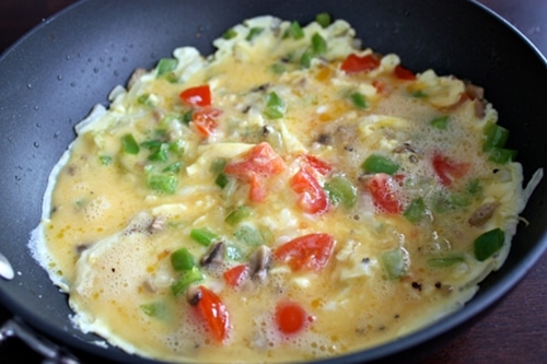 Whipped eggs poured with ingredients in skillet. 