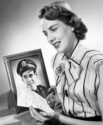 Vintage woman reading handwritten letter from soldier in front of his photo frame.