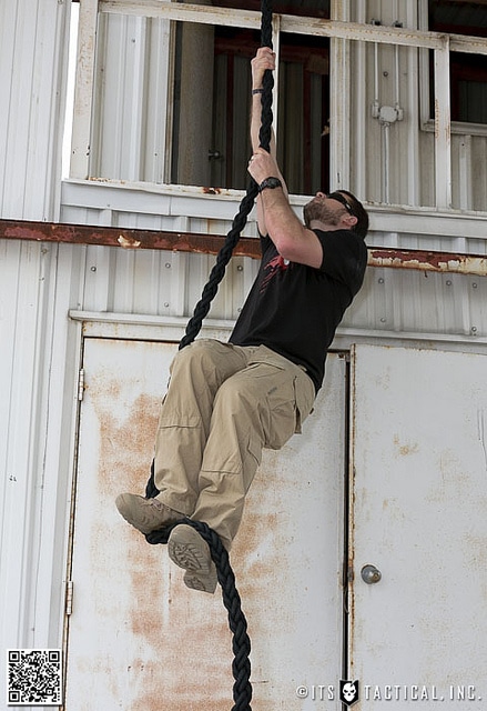 Man climbing a rope like a seal in warehouse.