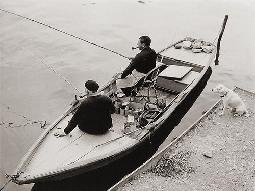 Uomini vintage in barca da pesca che fumano pipe vicino al molo.