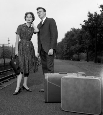 Vintage couple standing near train tracks with luggage.