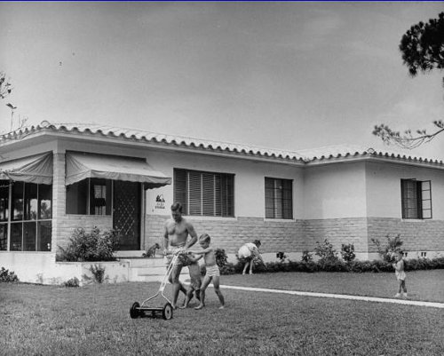 Vintage man pushing reel mower with little child.