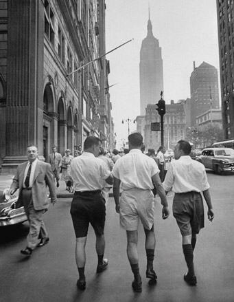 Men wearing shorts walking down the street.