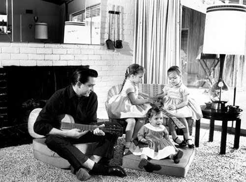 Vintage a man sitting with three little children's and playing guitar.