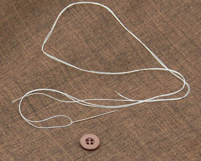 Button and white thread with needle on a brown cloth.