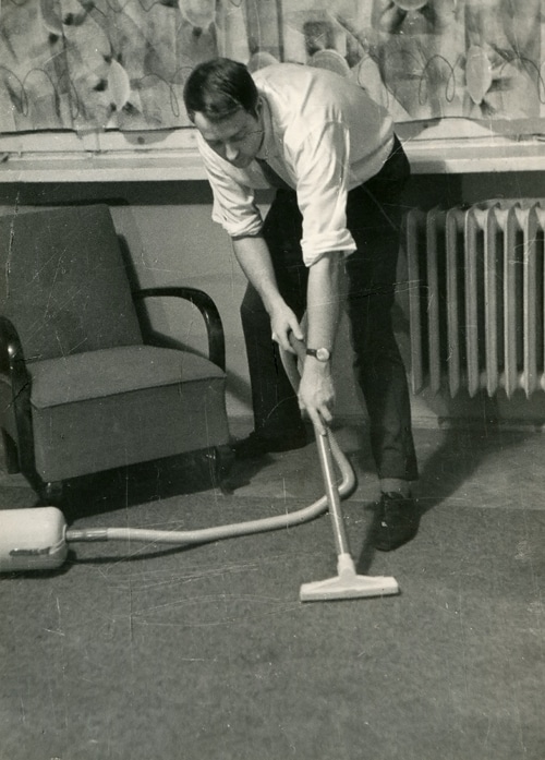 Vintage man vacuuming floor business clothes.