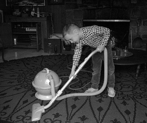 Vintage young boy vacuuming floor doing chores. 