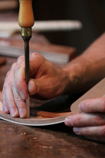 Luthier guitar maker working on curved wooden panel. 