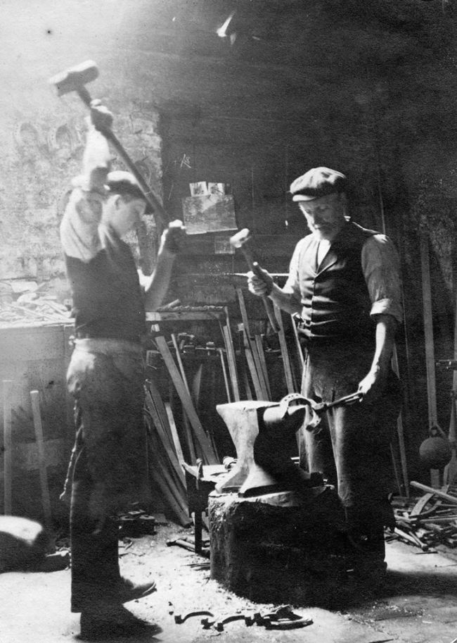 Vintage blacksmiths in workshop hammering on anvil.