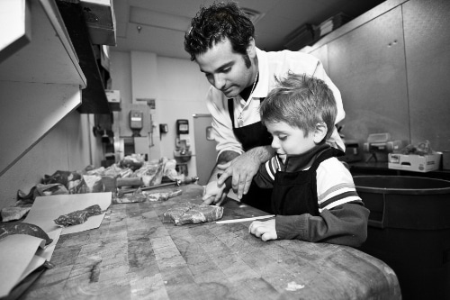 Danny Catullo butcher showing young boy how to cut meat.