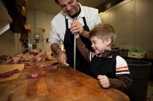 Danny Catullo butcher showing young boy to sharpen knife.