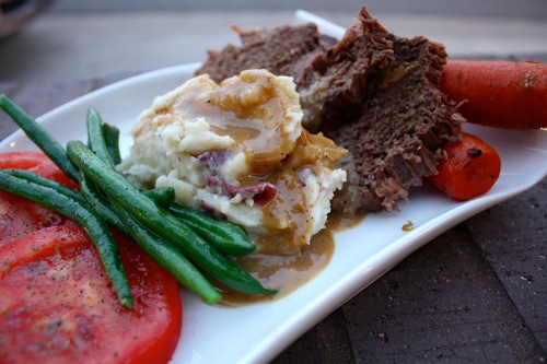 Meat potatoes gravy green beans carrots on plate. 