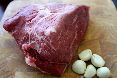 Slow roast beef ingredients raw red meat garlic on cutting board. 