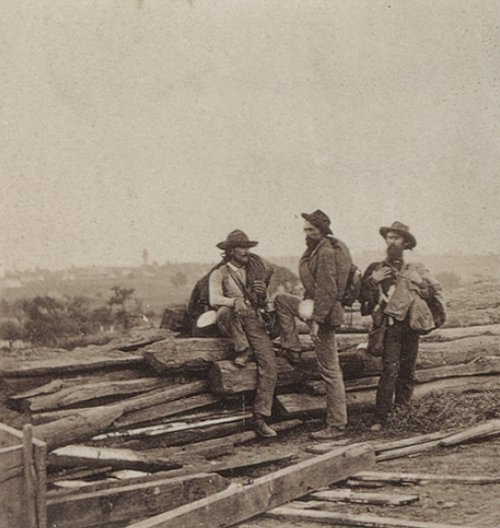 Confederate soldiers standing around broken down building in civil war. 