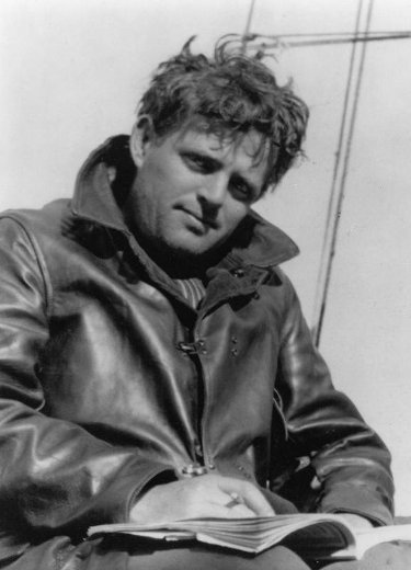 Jack London in leather jacket sitting outdoor writing in notebook with ruffled hair. 