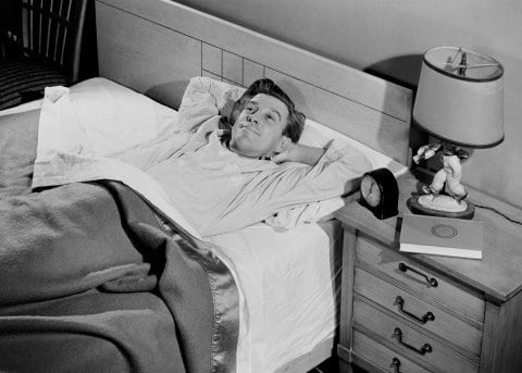 Vintage young man in bed awake with smile and cheery face.