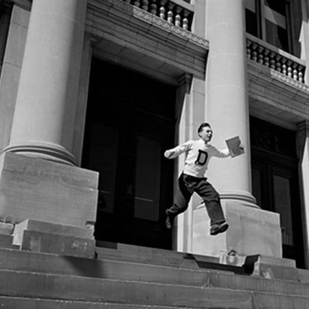 Vintage young man running down stairs with diploma. 