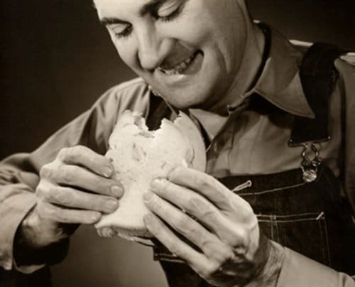 Vintage man eating sandwich with smile on face. 