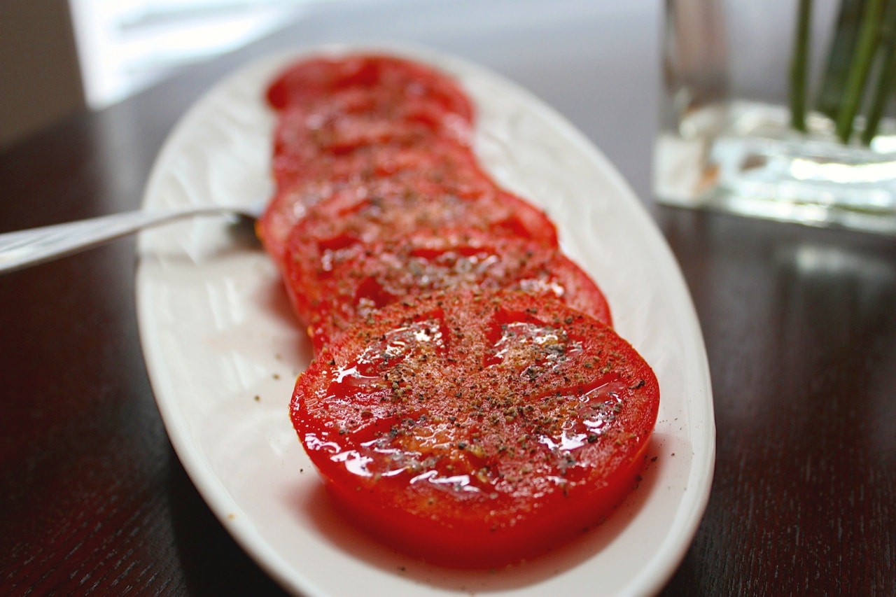 Sliced fresh red tomatoes with pepper seasoning .