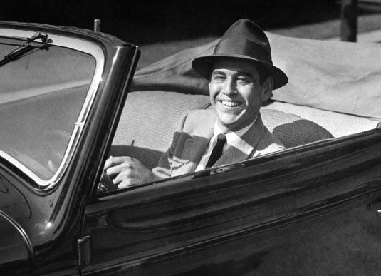 Vintage man in convertible smiling wearing hat.