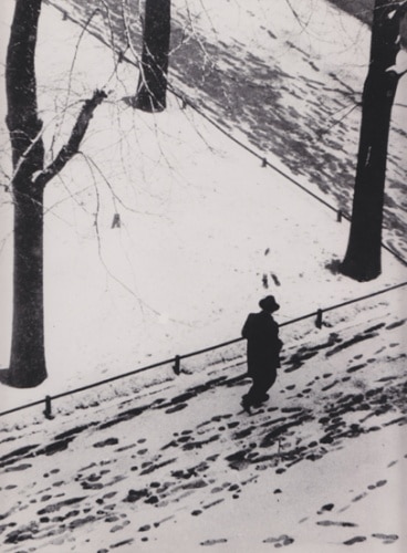 Vintage man walking along in snow on street sidewalk.