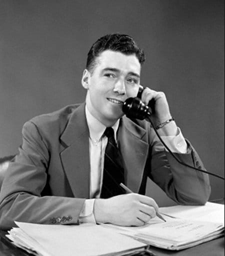 Vintage young businessman at desk with paperwork on phone.