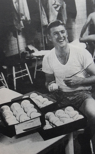 Vintage baseball player in locker room signing baseballs.