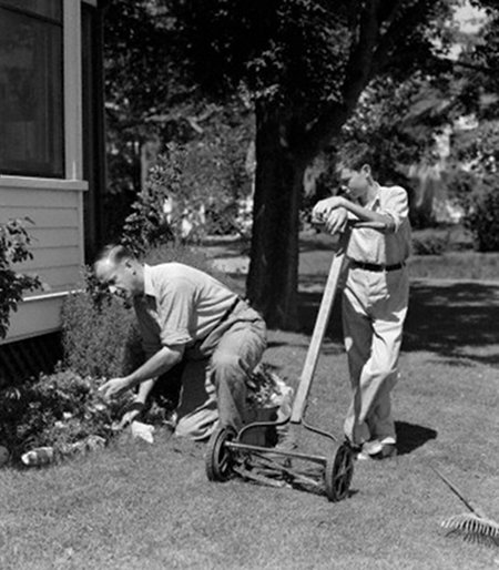 Vintage boy mowing lawn with reel mower father doing gardening.