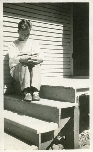 Vintage man reading book on lap on steps of house. 