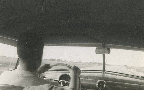 Vintage man in interior of car driving at down road . 