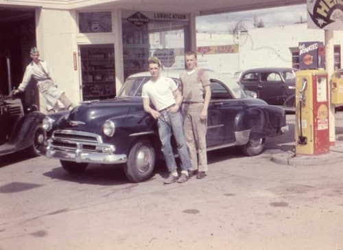 Men posing in front of car at gas station .