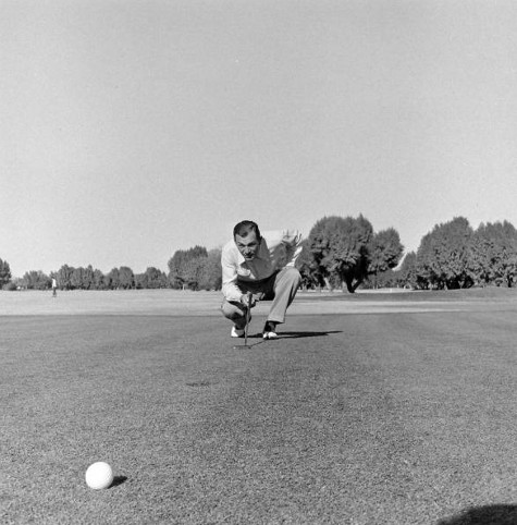 Vintage golfer on green looking at hole bale foreground.