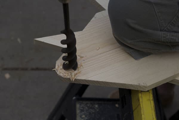 Man using pull saw on piece of wood board auger end piece.