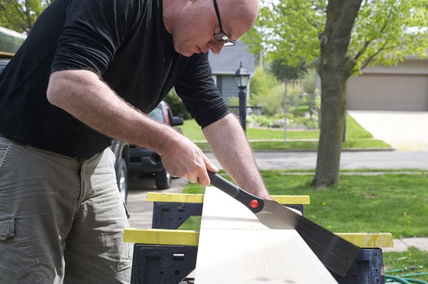 Man sawing board on sawhorses with saw.