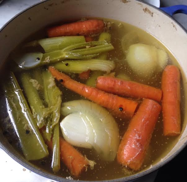 Homemade diy chicken stock in large pot with celery carrots onions.
