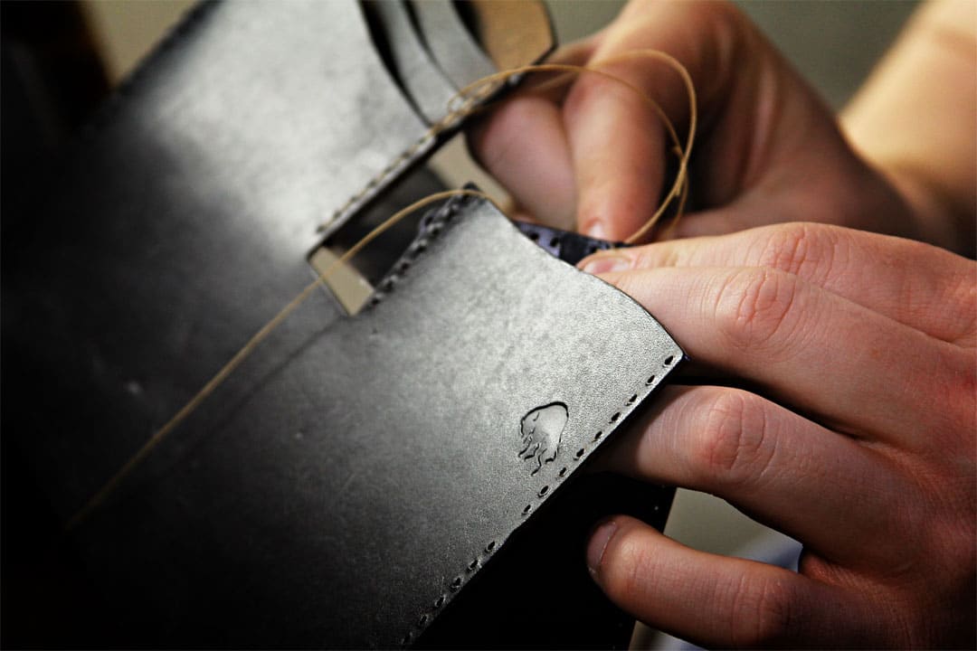 Black leather wallet being hand stitched close up photo.