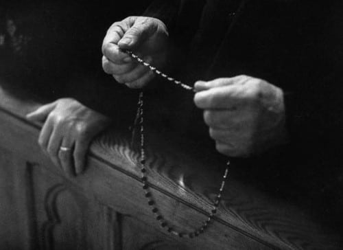 Man holding rosary in hands black white photo close up.