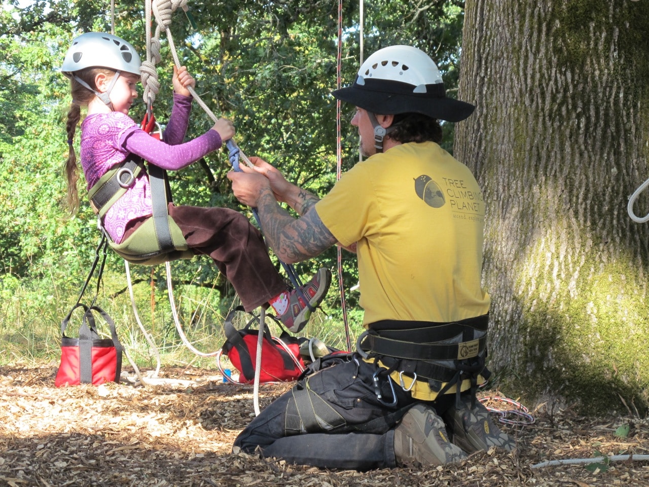 Men helping to a little girl for tree climbing.