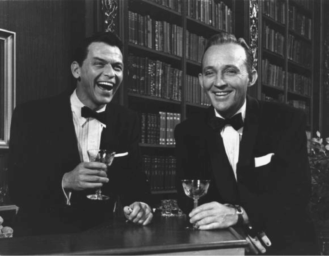 Sinatra drinking gin martini at a bard tuxedo laughing.