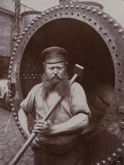 A long beard vintage blue collar worker with large sledgehammer.